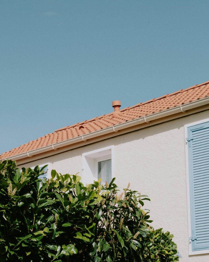 A charming house facade with blue shutters and a terracotta roof under a clear sky.